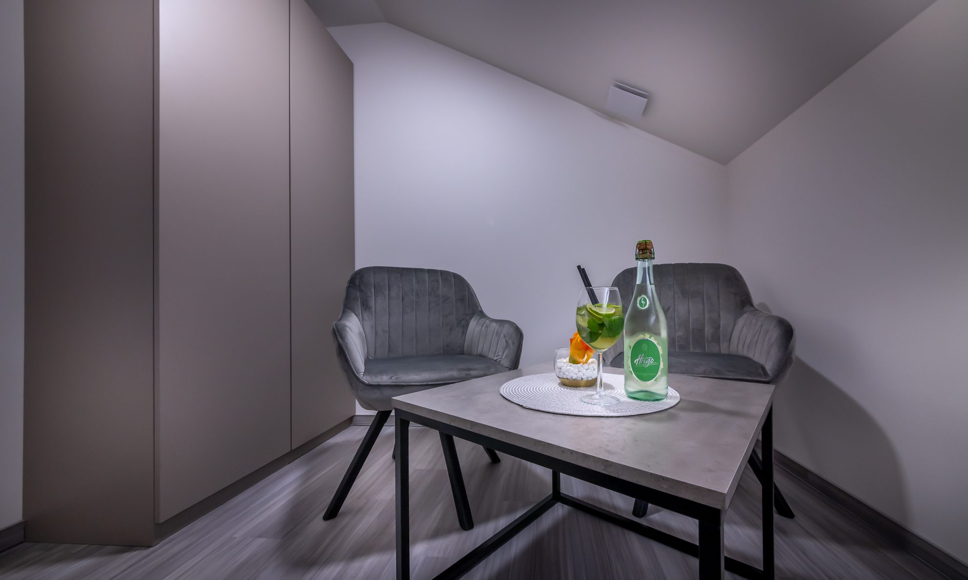 Koktajla na mizi med dvema sivima foteljema, kotiček sobe S-Center