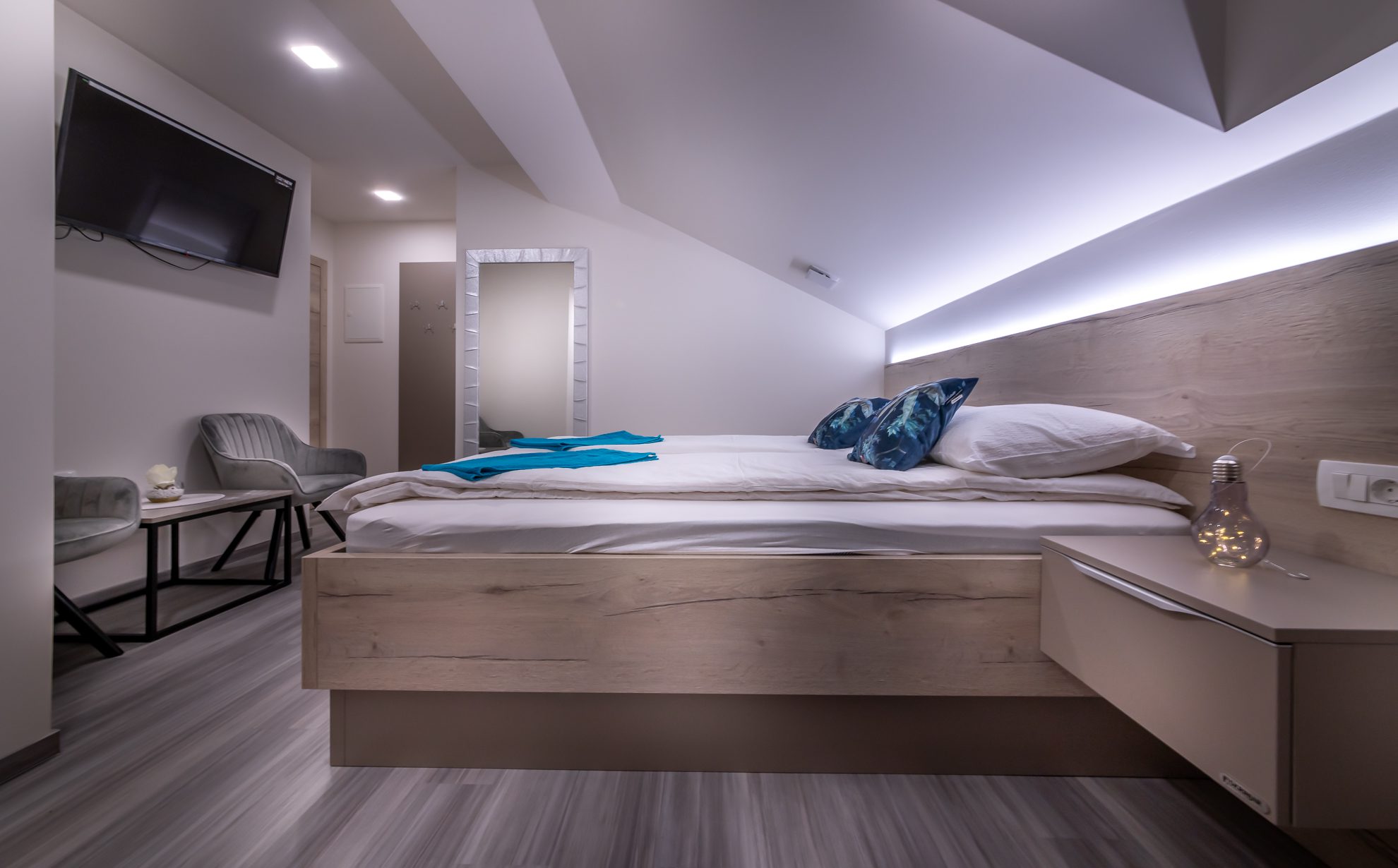 Soba S-Center v topli večerni svetlobi z belo posteljnino in modrimi blazinami