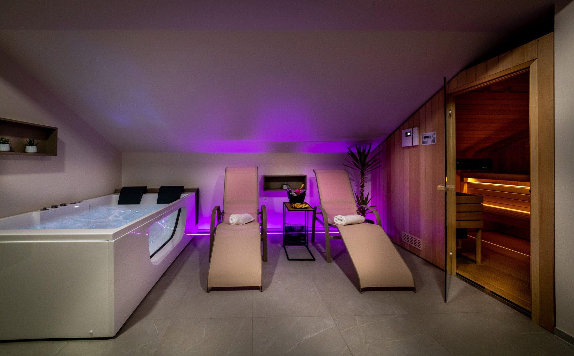 Isti wellness prostor S-Center v vijolični svetlobi — kad, ležalnika in vhod v savno